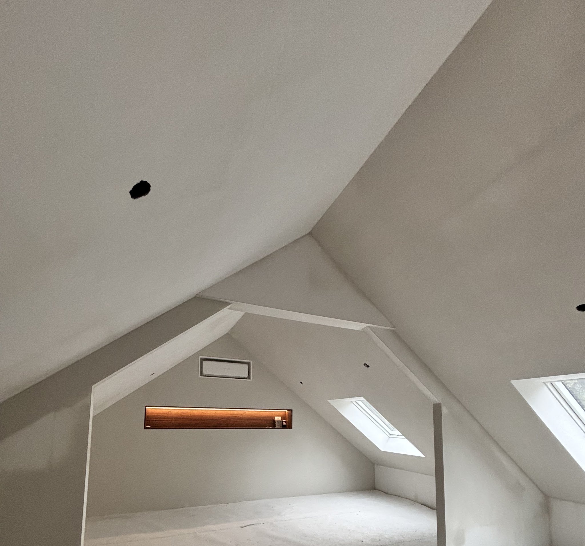 Gestucte zolder met schuine wanden, twee dakramen en een verlichte nis in de achterwand