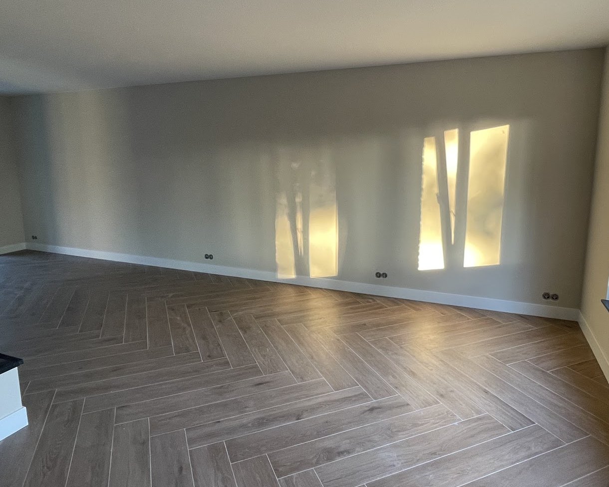 Gladde, lichte woonkamerwand met zonlicht dat door het raam op het stucwerk valt, boven een visgraatvloer