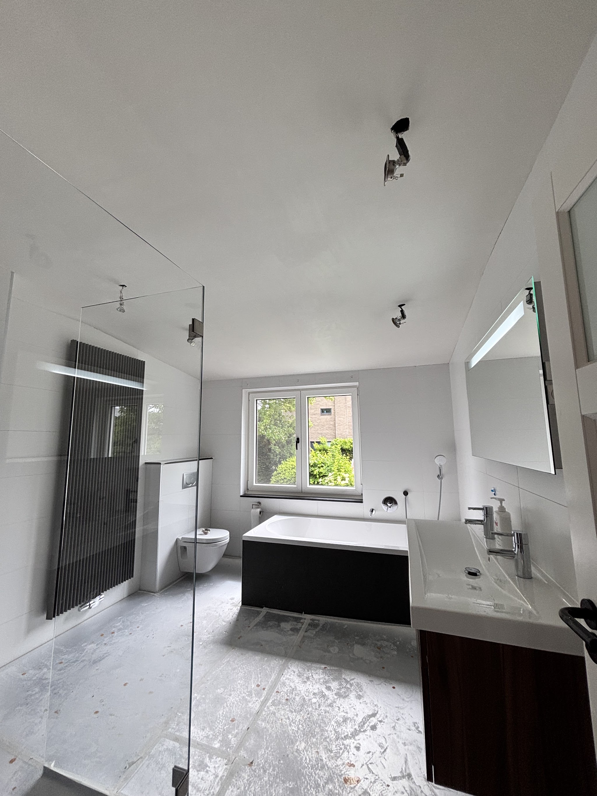 Badkamer met strak gestucte wanden, een glazen douchewand, een bad en een wastafelmeubel